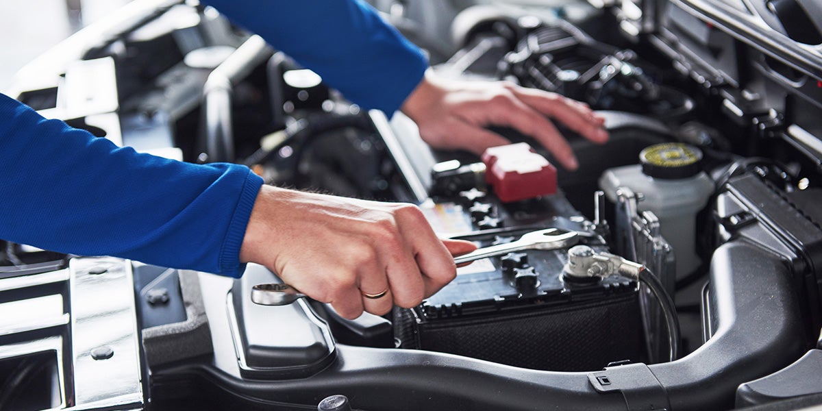 A mechanic using a wrench to adjust a connection on a car battery under the hood of a vehicle.